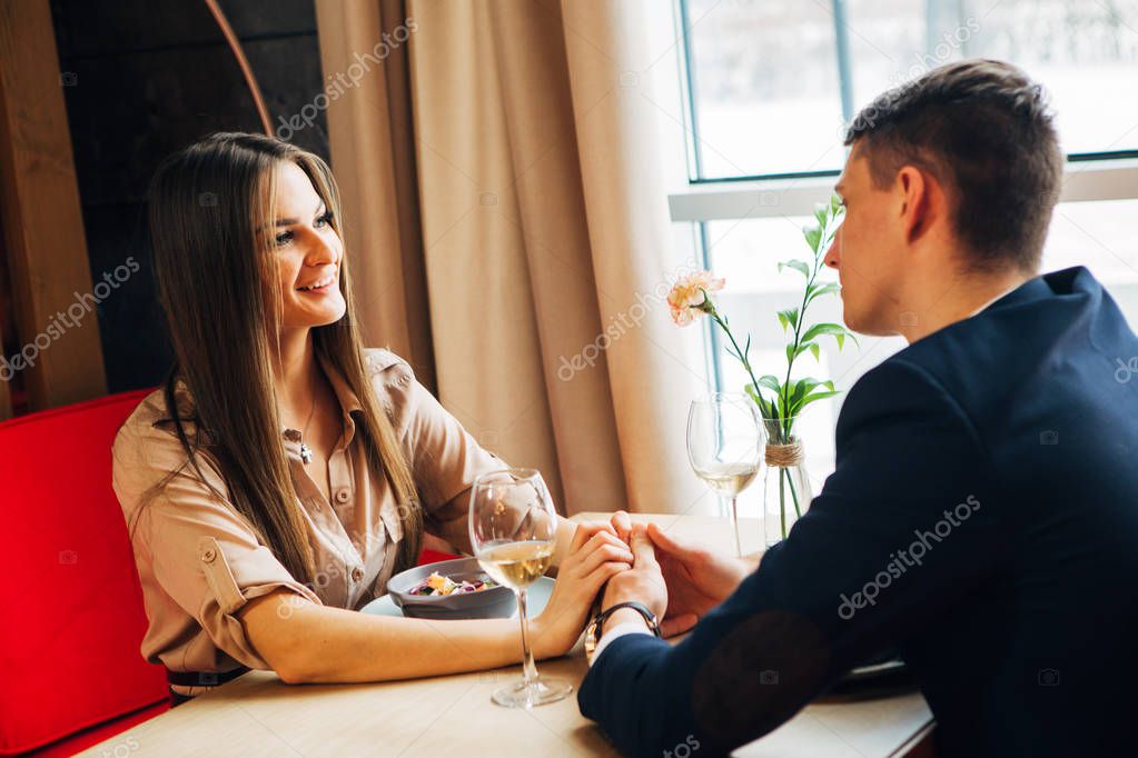 Young happy couple romantic date drink glass of white wine at restaurant, celebrating valentine day