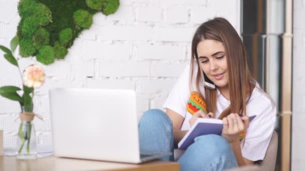 De vrouw van een jonge freelancer met een notitieboekje en laptop werkt in een café. — Stockvideo