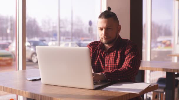 Hipster barbudo trabalhando em um laptop em um café — Vídeo de Stock