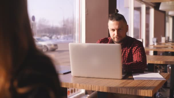 Молодой бородатый бизнесмен сидит за столом в кафе. На настольном ноутбуке. Человек работает, учится. Онлайн-образование, маркетинг, обучение — стоковое видео
