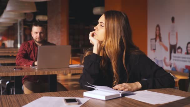 Втомлена молода бізнес-леді сидить за столом з блокнотом — стокове відео