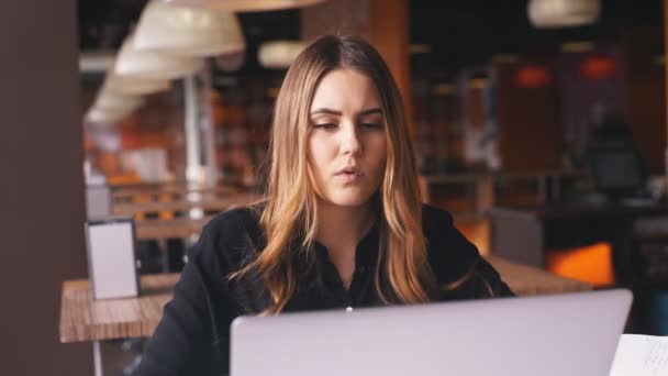 Seriös affärskvinna i en svart tröja som arbetar på en bärbar dator och tar anteckningar i en anteckningsbok — Stockvideo