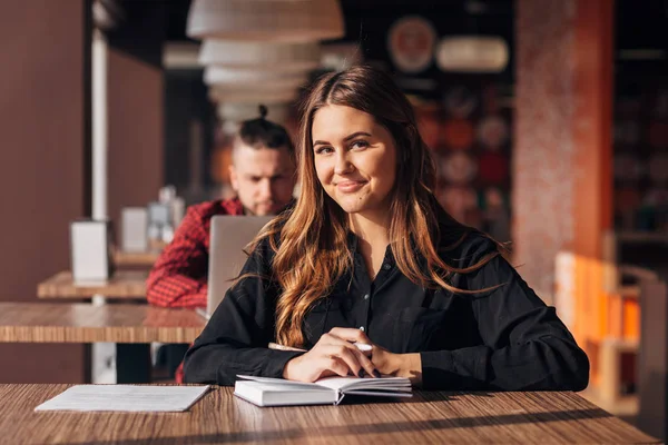 Feliz mujer de negocios sentada en un café con un cuaderno y sonriendo a la cámara —  Fotos de Stock