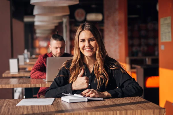 Femme d'affaires assis à la table dans un café avec ordinateur portable tout en montrant pouce vers le haut et en regardant la caméra — Photo