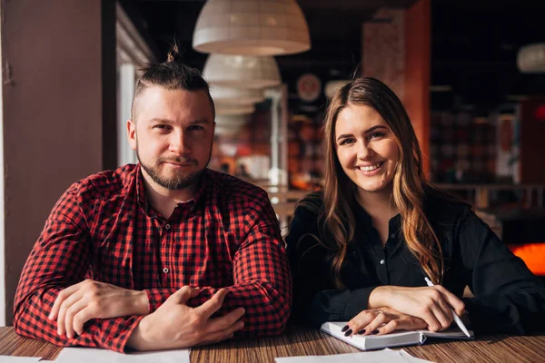 Happy businesswoman and her colleague looking at camera while working in cafe