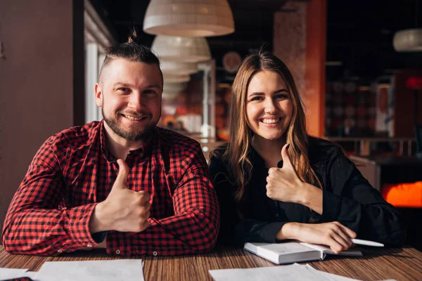 Deux pigistes heureux sourire à la caméra dans le café doigt vers le haut, bon travail — Photo