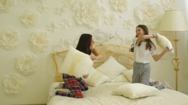 Mutlu aile anne ve kızı yatak ve yastık savaşında oynuyorlar.