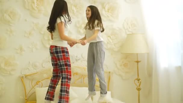 Красивые мама и дочь веселятся во время прыжка на кровати дома — стоковое видео
