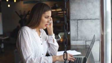 Laptop ile çalışan ve müşteri pencere oturmak için konuşmak smartphone cep telefonu ile konuşmak güzel genç kadın