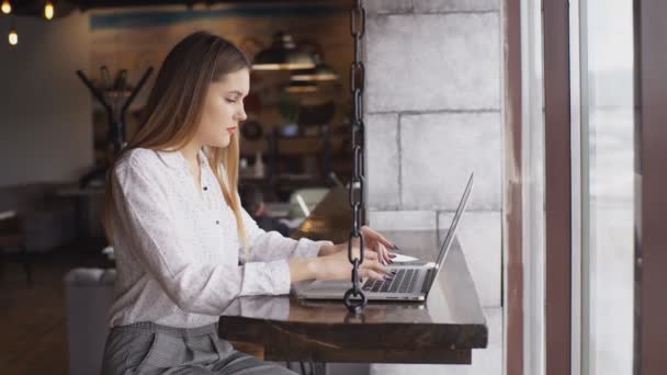 Hermosa mujer de negocios en una camisa blanca que trabaja en un ordenador portátil en un café — Vídeos de Stock