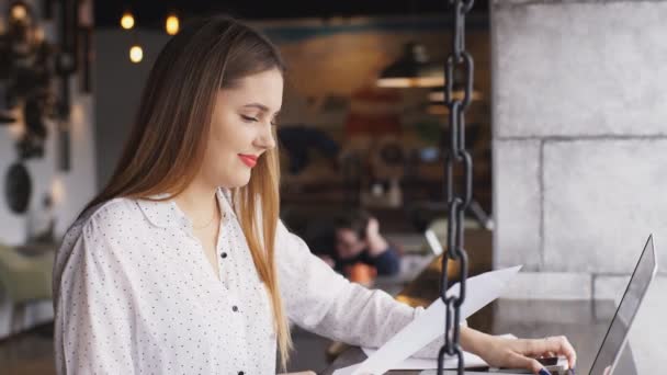 Bela mulher de negócios em uma camisa branca trabalhando em um laptop em um café — Vídeo de Stock