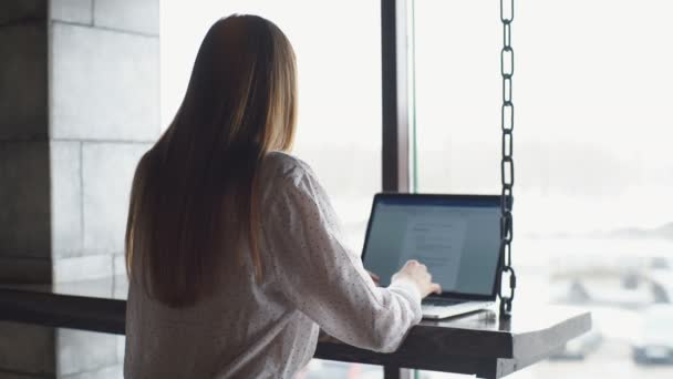 Giovane donna d'affari vestita in camicia bianca è seduto in caffè al tavolo di legno di fronte al computer portatile e parlando sul cellulare . — Video Stock
