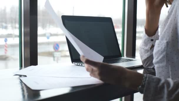 La joven empresaria trabaja en la cafetería con el portátil, firma los documentos y habla por teléfono — Vídeo de stock