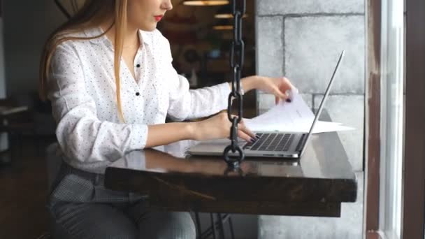 Young business woman working on a laptop holding documents in hands — Stock Video