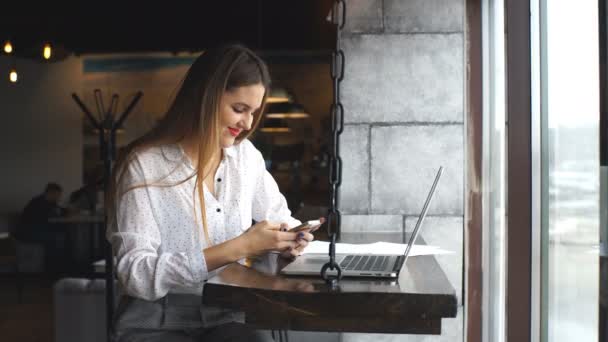 Sonriente mujer de negocios escribiendo en su portátil y utiliza un teléfono inteligente — Vídeos de Stock