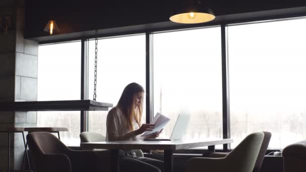 Jovem empresária trabalhando em um laptop segurando documentos nas mãos — Vídeo de Stock