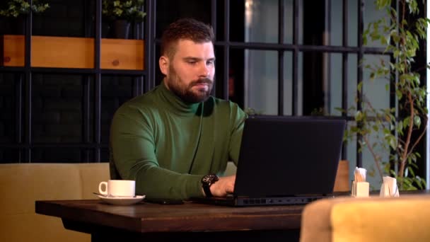 Ung attraktiv skäggig man tryggt arbetar på laptop under kaffepausen i caféet — Stockvideo