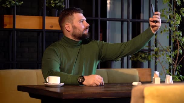 Bebaarde hipster neemt een selfie in een cafe — Stockvideo