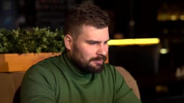 Vahşi sakallı bir adam bir kafede oturuyor ve bir dizüstü bilgisayar üzerinde çalışıyor.