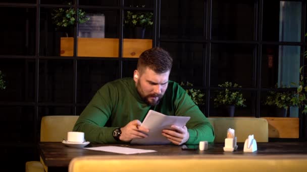 Vousatý hipster podepisuje papíry sedí v kavárně — Stock video