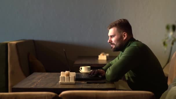 O homem está satisfeito com o trabalho feito. Jovem feliz trabalhando em um laptop enquanto está sentado em um café — Vídeo de Stock