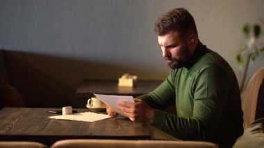 Sakallı hippi bir kafede oturan kağıtları imzalıyor.