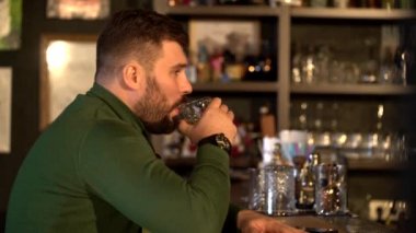 Sakallı bir adam barda oturmuş viski içiyor ve telefonda kız arkadaşıyla mesajlaşıyor.