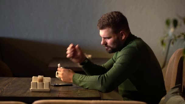 Un hombre se pone auriculares en los oídos en un café y escucha su música favorita — Vídeos de Stock