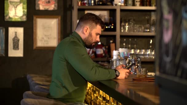 Hipster cansado bebe uísque em um bar e textos — Vídeo de Stock