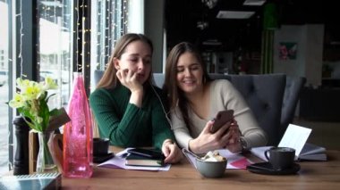 İki kadın gün boyunca bir kafede oturup akıllı telefondan video izlerler..
