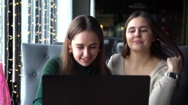 İki duygusal pozitif tatlı arkadaş öğle yemeği yiyor, kafede oturuyor, dizüstü bilgisayar kullanıyor.