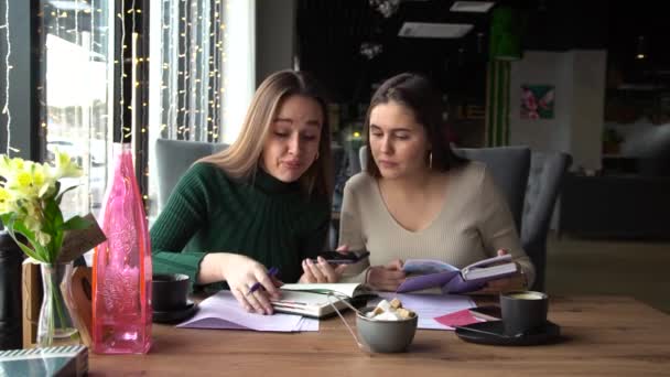 İki genç iş kadını bir kafede oturmuş hoparlörde partnerleriyle konuşuyorlar. — Stok video