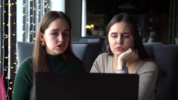 Dos jóvenes empresarias están sentadas en una mesa en un café con portátil — Vídeo de stock