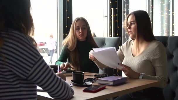 Cuatro jóvenes agentes sentados en la cafetería, discutiendo papeles y organizando el trabajo — Vídeos de Stock