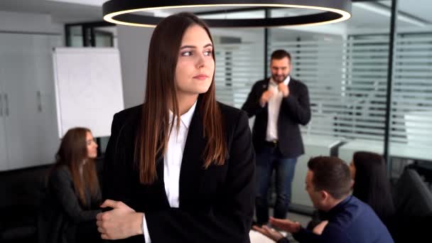 Una donna d'affari alla telecamera. si alza con le braccia incrociate davanti ai suoi colleghi, che sono seduti ad un tavolo dietro di lei . — Video Stock