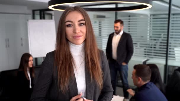 Mujer de negocios de pie en un moderno edificio de oficinas con colegas en el fondo — Vídeos de Stock