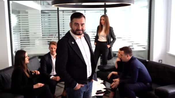 Porträtt av affärsman i modernt kontor med kollegor möte runt bordet i bakgrunden — Stockvideo