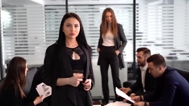 Сексуальная деловая женщина смотрит в камеру с сотрудниками позади — стоковое видео