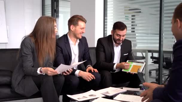 Eine Gruppe von Arbeitern, die an einem Tisch in einem Konferenzraum sitzen, lachen und tauschen sich mit ihren Kollegen über ein neues Projekt aus — Stockvideo