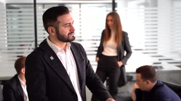 Egy szakállas üzletember figyelmesen néz ki az ablakon, egy üzleti találkozó hátterében — Stock videók
