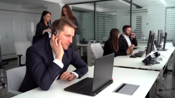 Un joven atractivo trabajando en un centro de llamadas con sus colegas — Vídeos de Stock