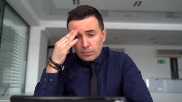 Un hombre reflexivo está trabajando en un ordenador portátil y hablando a través de un enlace de vídeo — Vídeos de Stock
