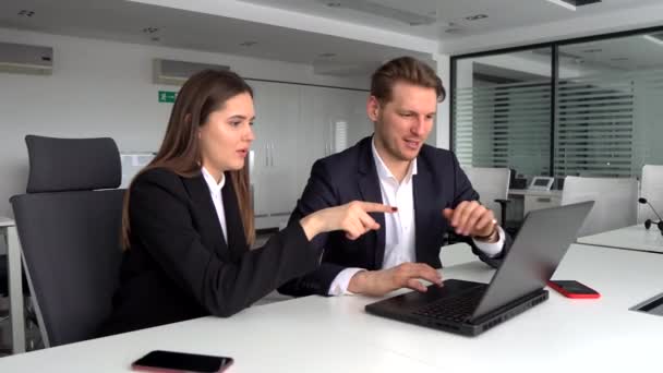 Colegas de negocios sentados en una mesa en una oficina moderna, hablando juntos sobre un ordenador portátil — Vídeo de stock