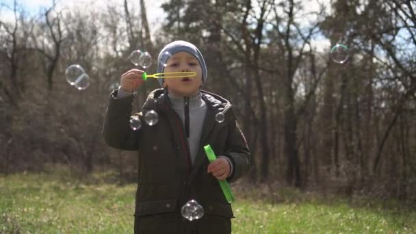 Mały chłopiec dmuchanie bańki mydlane w parku. slow-mo — Wideo stockowe