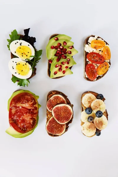 Beyaz arka planda altı farklı kadeh kaldırma. Yumurta, meyve ve böğürtlen, avokado ve domatesli çeşitli tostlar..