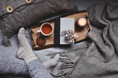 Kadın bacakları, bir fincan çay, ekose ve mumla rahat bir ev.  