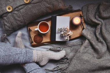 Kadın bacakları, bir fincan çay, ekose ve mumla rahat bir ev.  