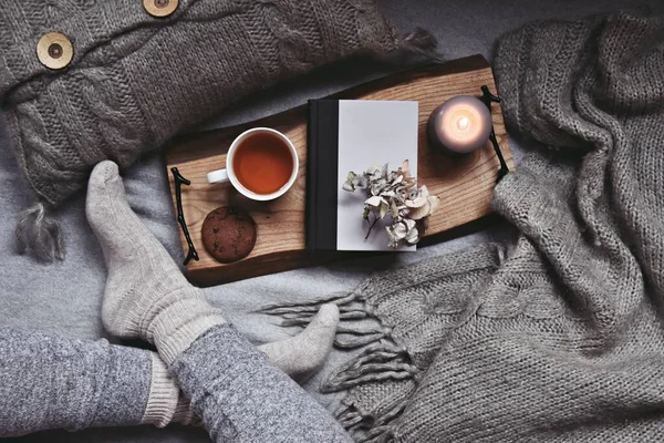 Kadın bacakları, bir fincan çay, ekose ve mumla rahat bir ev.  