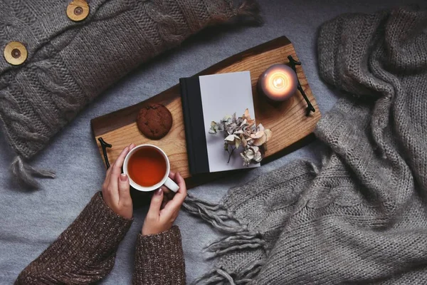 Kadın ellerinde çay, ekose ve mumla rahat bir ev.  