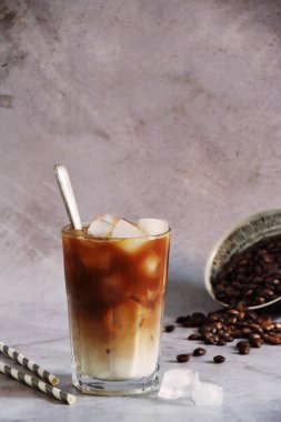 Büyük bardakta buzlu kahve ve krema dökülmüş kahve çekirdekleri eski bir ahşap tahta üzerinde. Karanlık ahşap arka planda fotokopi alanı olan soğuk yaz içeceği.